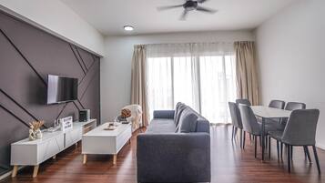 A modern living room with a sofa, dining table, and chairs, a TV mounted on the wall, and a ceiling fan.
