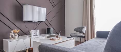 Una sala de estar moderna con un televisor de pantalla plana montado en una pared con diseño geométrico, una mesita blanca con una bandeja, un sofá gris y un sillón gris.