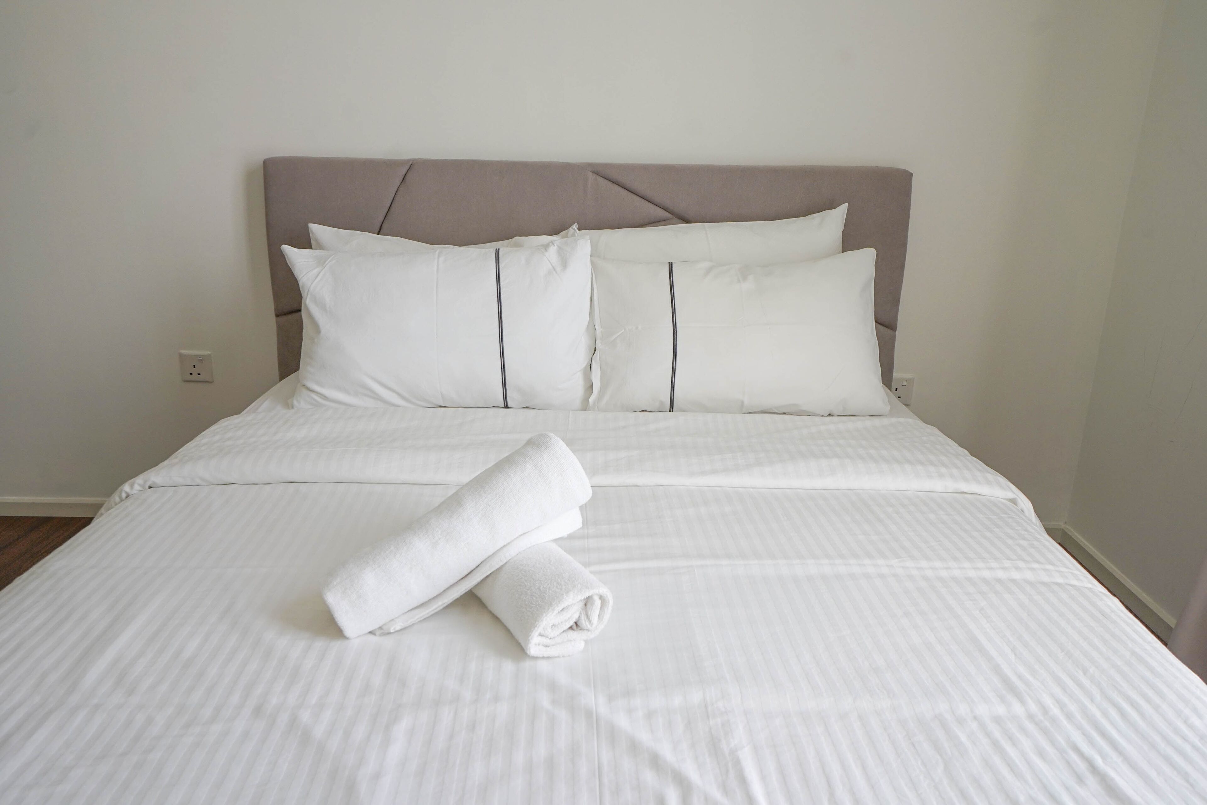 Una cama bien hecha con sábanas y almohadas blancas, una toalla doblada sobre la cama y un cabecero con diseño geométrico.