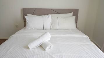 Una cama bien hecha con sábanas y almohadas blancas, una toalla doblada sobre la cama y un cabecero con diseño geométrico.