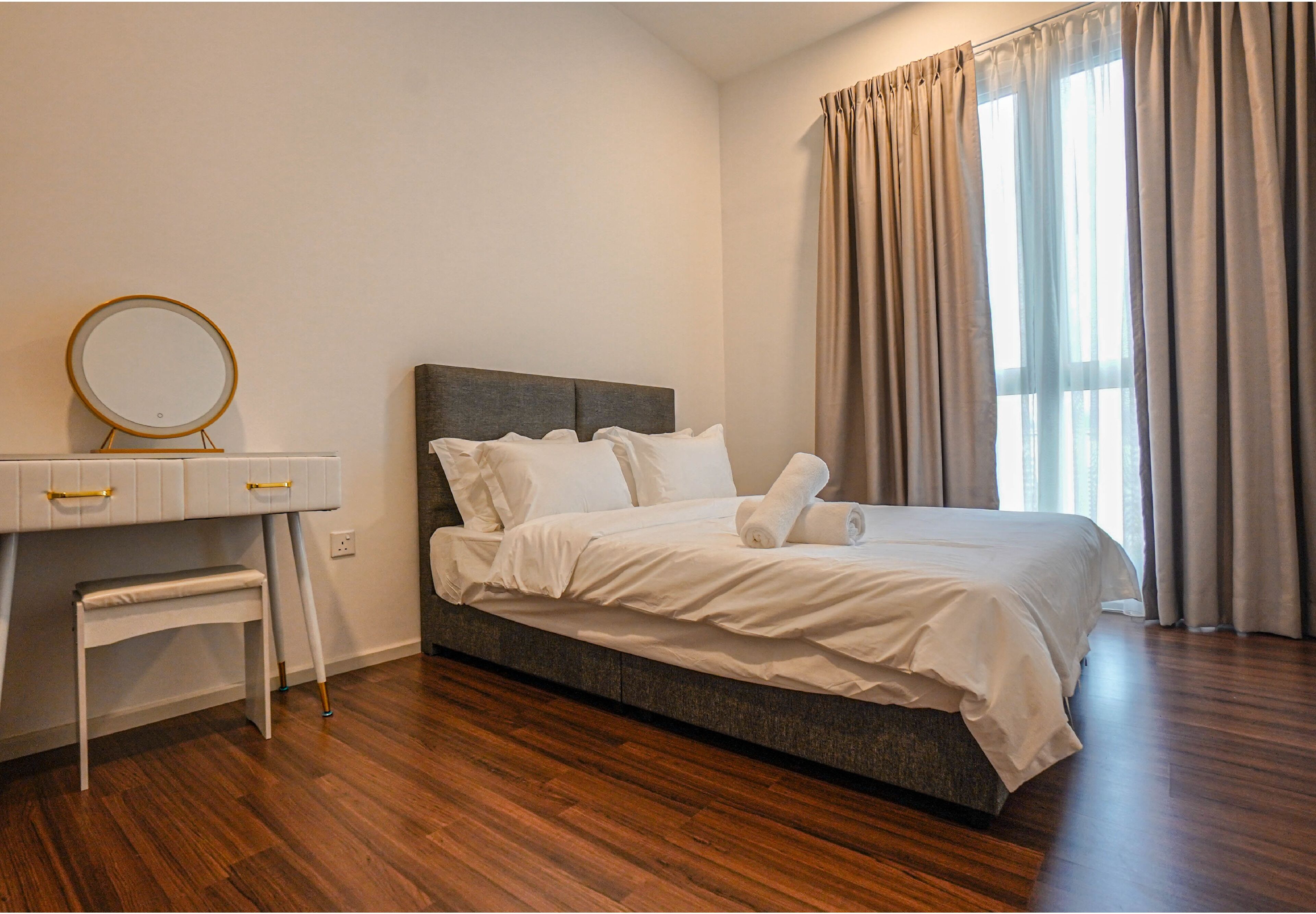 A bedroom with a bed, a bedside table with a mirror, a bench, and a window with curtains.