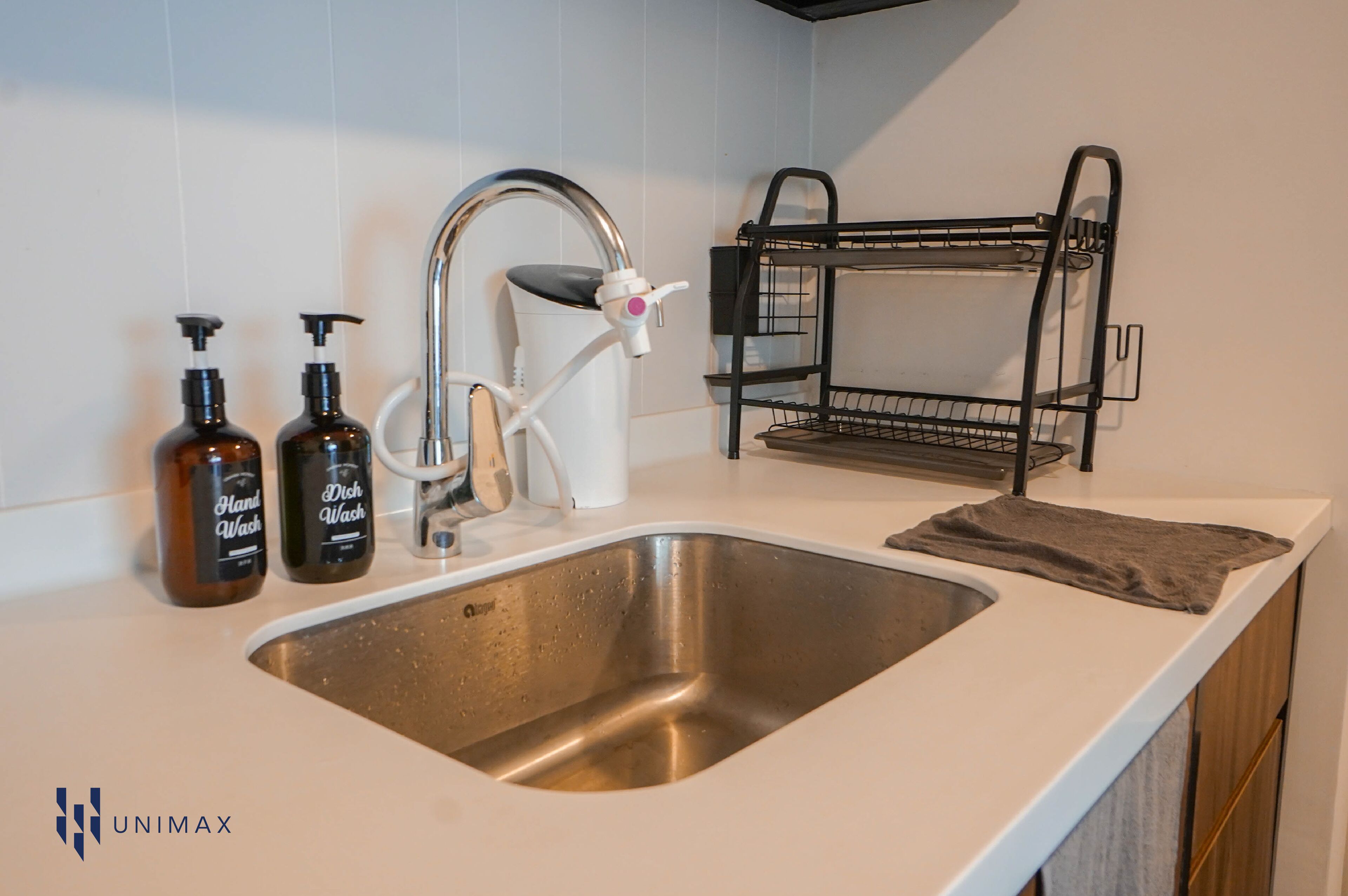 A kitchen with a stainless steel sink, a white faucet, and two hand wash bottles.