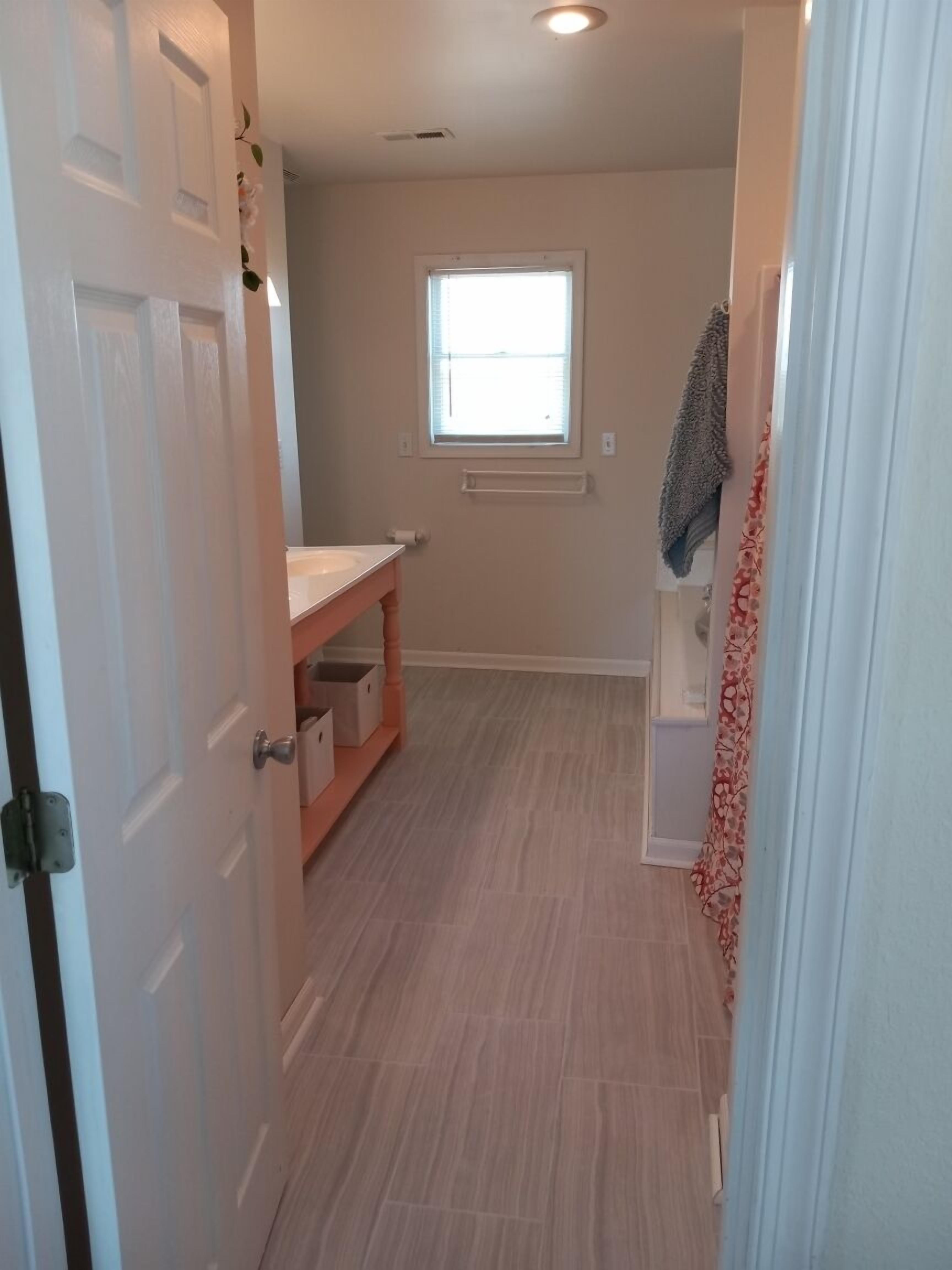 A narrow hallway with a wooden floor, a window with blinds, and a door with a towel hanging on it.