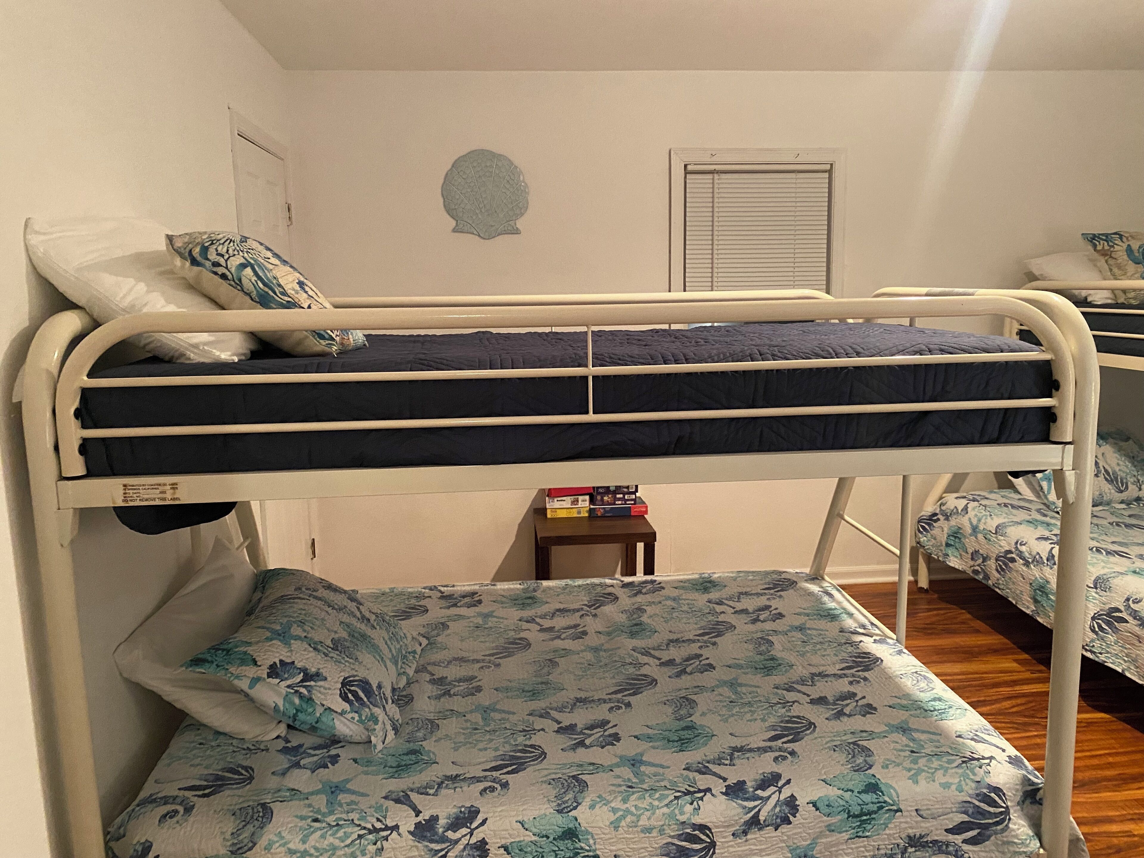 A bunk bed with floral bedding, a small bedside table with books, and a wall decoration.