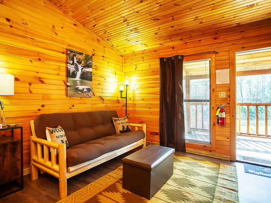 A wooden cabin interior with a sofa, a small table, a lamp, and a painting of a waterfall.