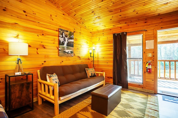 A wooden cabin interior with a sofa, a small table, a lamp, and a painting of a waterfall.