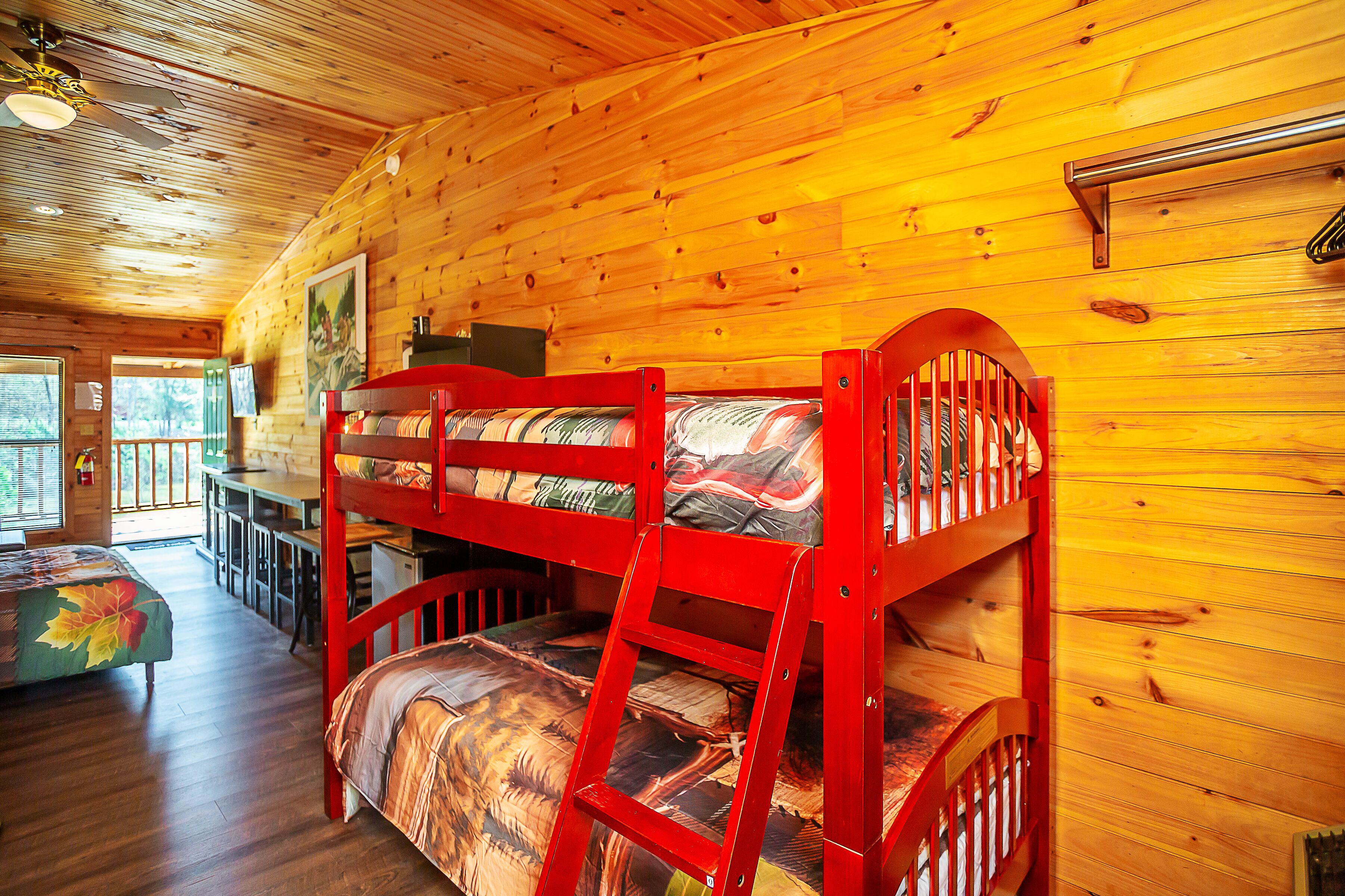 Une cabane aux murs et au plancher en bois, un lit superposé avec une échelle, une table à manger et une fenêtre donnant sur les arbres.