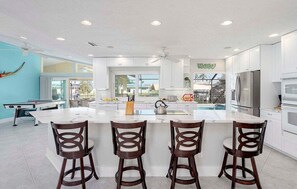 Una cocina moderna con armarios blancos, una isla grande con taburetes y vistas al exterior.