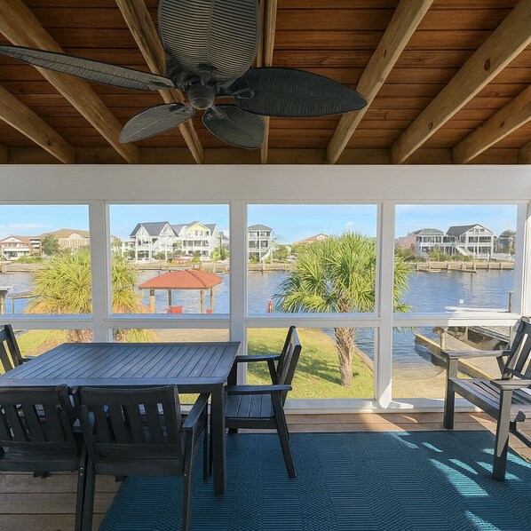 Patio esterno con tavolo e sedie, una ventola a soffitto e vista su case oltre un corso d'acqua.