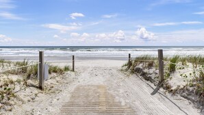 Ein Holzsteg führt zu einem Strand, gesichert durch ein Seil und Holzbalken.