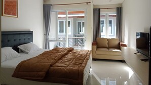 Una habitación de hotel con cama, sofá, televisión y balcón con cortinas.