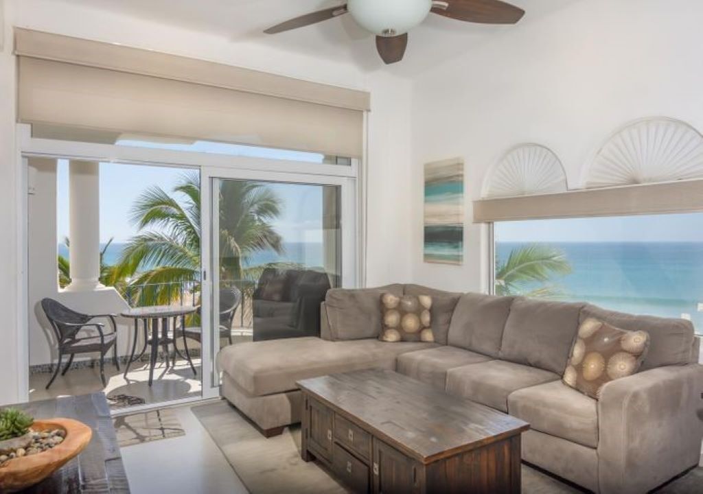 A living room with a beige sectional sofa, a wooden coffee table, and a dining area with a table and chairs. - Mykonos Bay Resort at Zippers Surf Break (San José del Cabo)