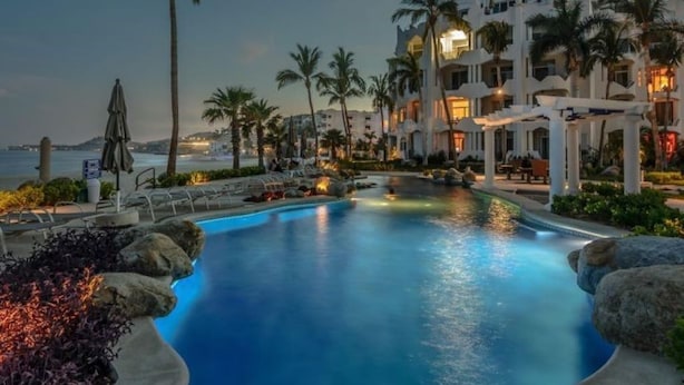 A pool area with a view of the ocean, surrounded by palm trees and a building with multiple balconies. - Mykonos Bay Resort at Zippers Surf Break (San José del Cabo)