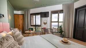 A bedroom with a large bed, a desk, a chair, a TV, and a view of the sea. - SEVEN Tel Aviv (Tel Aviv)