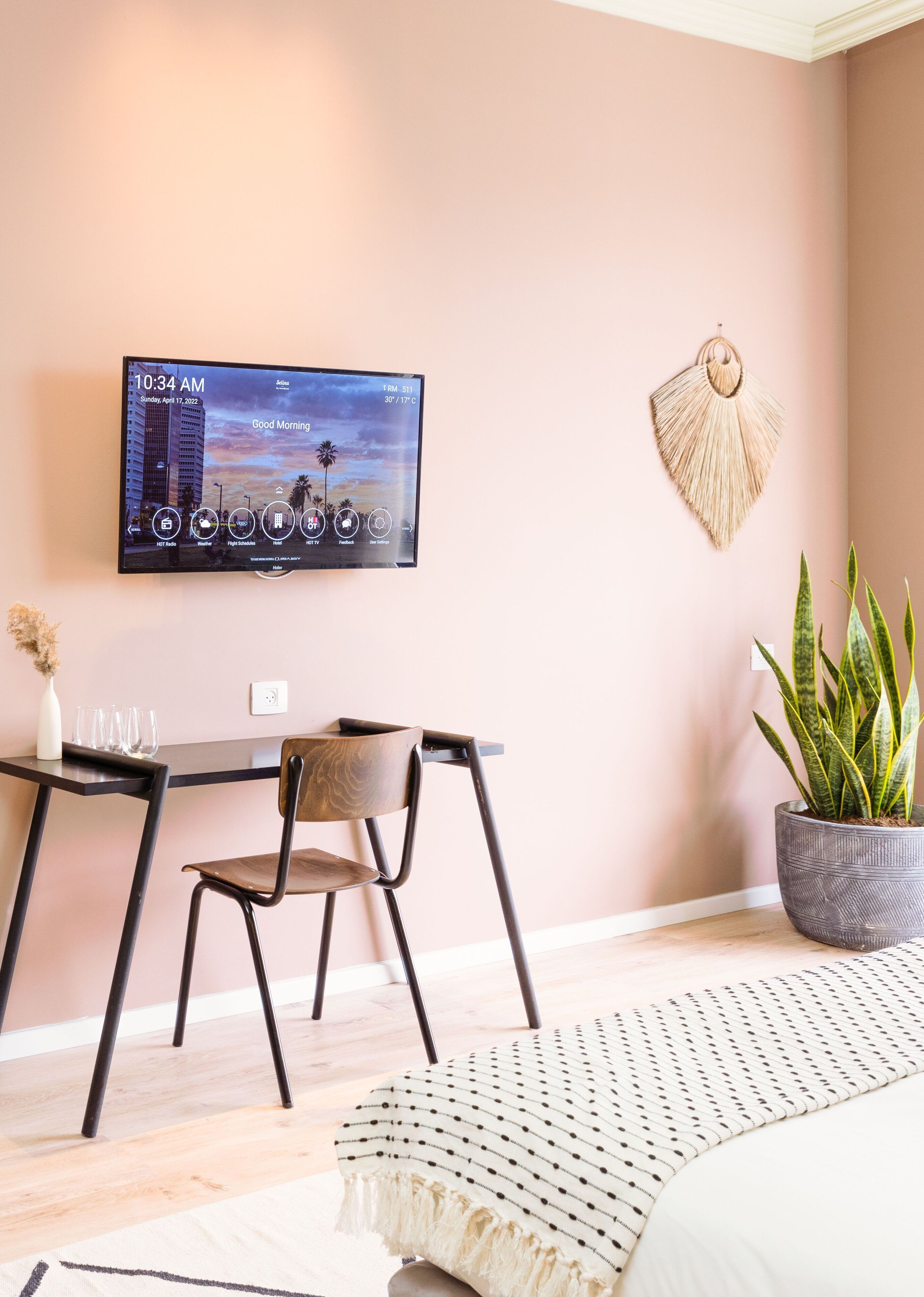 A modern room with a desk, chair, and a television mounted on the wall displaying the time and weather.