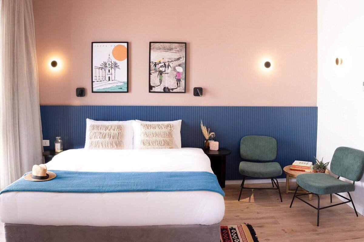 A bedroom with a bed, two wall-mounted lights, a framed picture, and a chair.