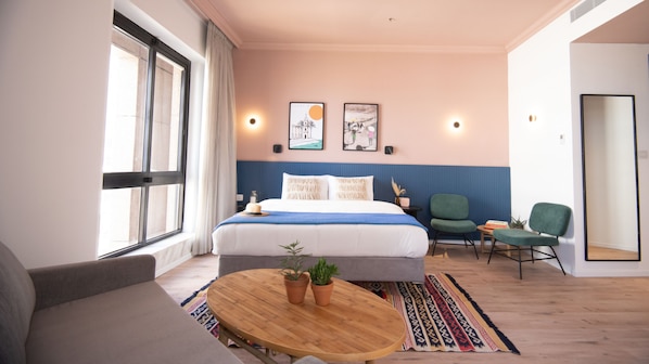 A modern hotel room with a large bed, a round wooden table, two green chairs, and a large window. - SEVEN Tel Aviv (Tel Aviv)