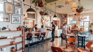 A café with a bar area, wooden chairs, and hanging plants. - SEVEN Tel Aviv (Tel Aviv)