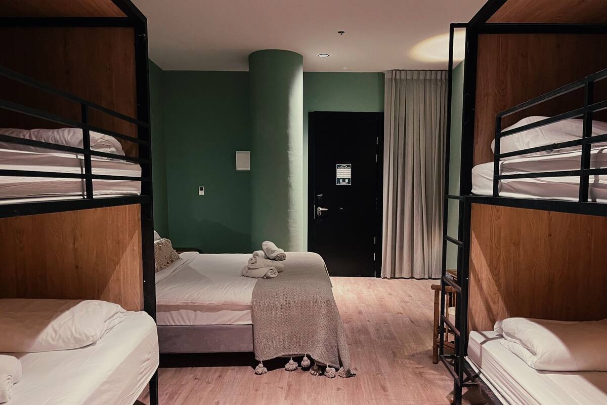 A room with bunk beds, a single bed, a door, and a curtain.