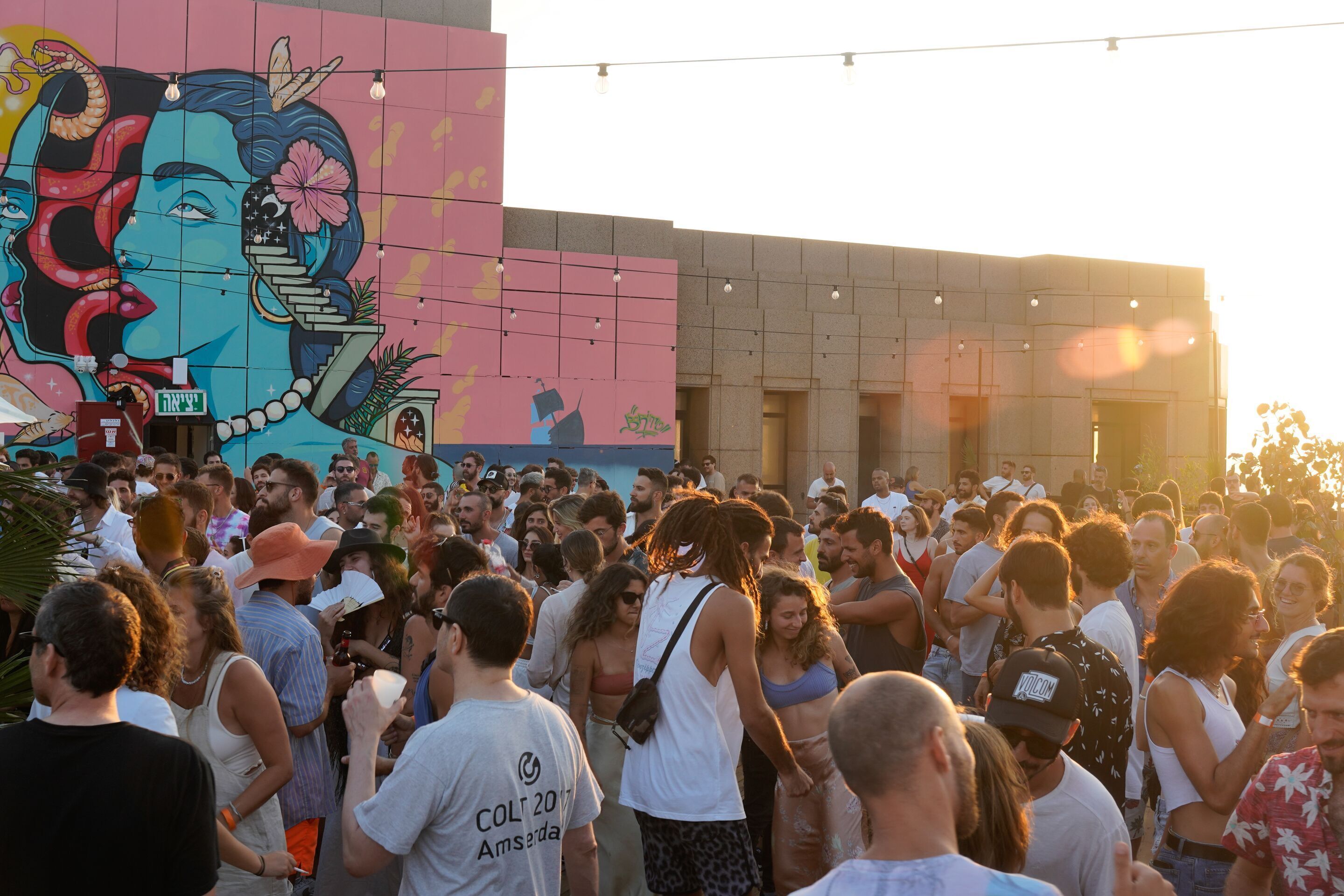 A crowded outdoor event with a large mural on a building in the background.