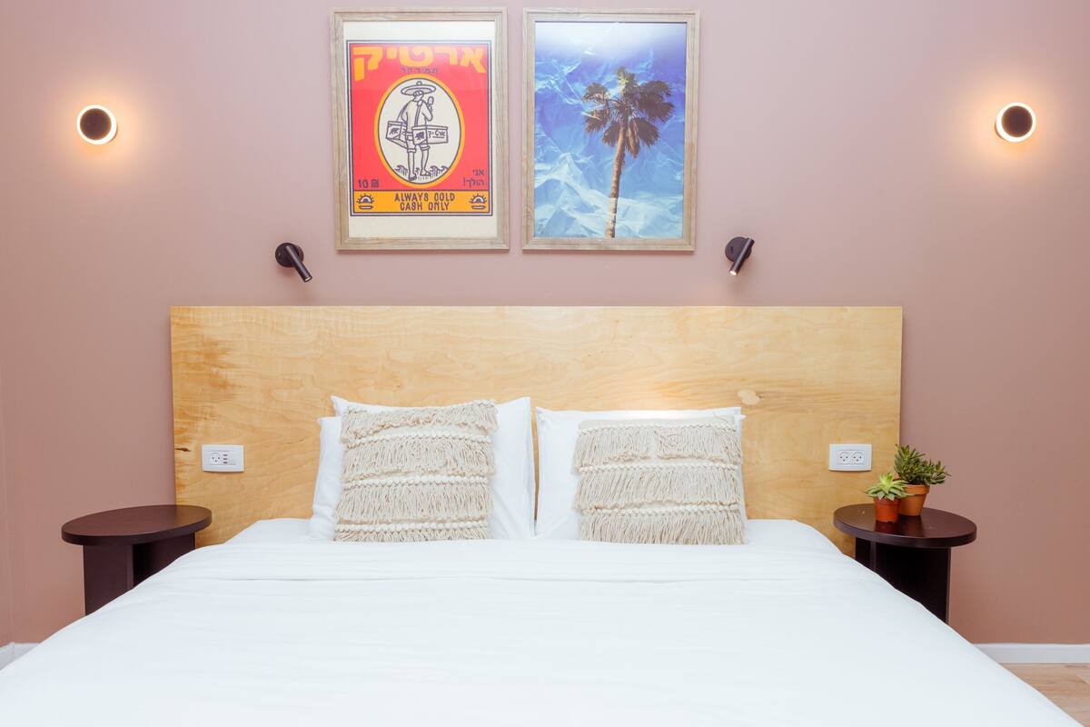 A neatly made bed with two pillows, a wooden headboard, and two bedside tables with small potted plants.
