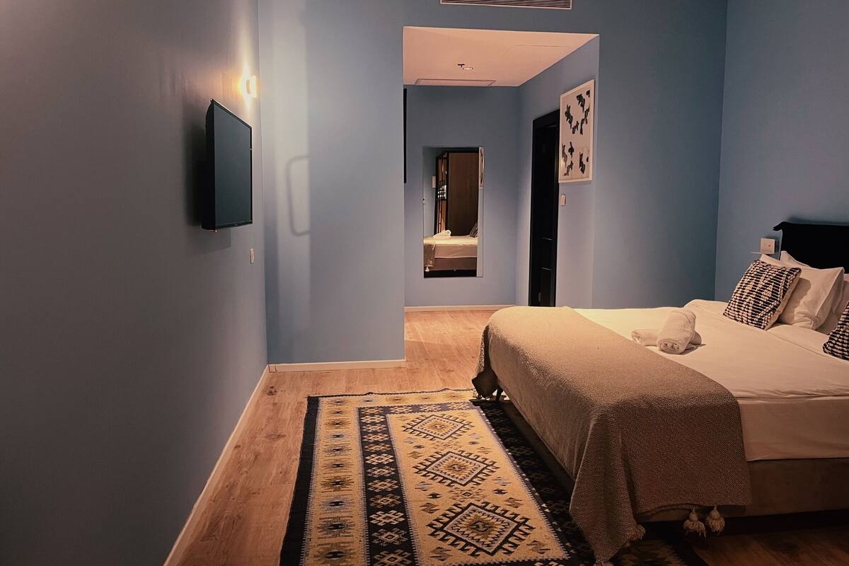 A bedroom with a bed, a TV mounted on the wall, and a door leading to another room.