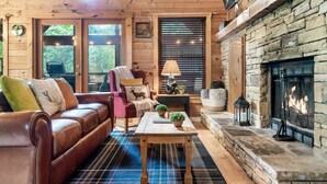 A cozy cabin interior with a fireplace, wooden walls, a leather sofa, and a plaid rug. - Hot Tub/Close2Downtown/Nearby Fishing Pond (Sevierville)