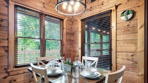 A wooden dining room with a table set for four, large windows, and a hanging light fixture. - Hot Tub/Close2Downtown/Nearby Fishing Pond (Sevierville)