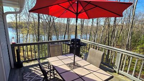 Um deck com mesa e cadeiras, um guarda-sol vermelho e vista para árvores e água.