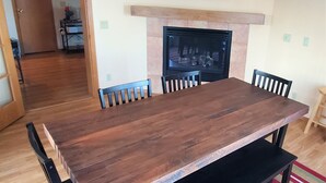 Uma sala de jantar com mesa e cadeiras de madeira, lareira e tapete listrado.