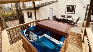 A covered deck with a hot tub, wooden deck, and a dining area with chairs and a table. - ZenNature with hottub & pet friendly (Tobyhanna)