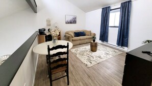 A living room with a sofa, a dining table with a chair, a small rug, and a window with curtains. - ZenNature with hottub & pet friendly (Tobyhanna)