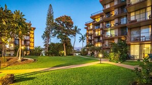 A hotel courtyard with a well-maintained lawn, pathways, and multiple-story buildings with balconies. - Kauhale Makai - Penthouse - Central AC -Oceanfront Unit - Ocean View! (Kihei)