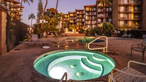 A hotel pool area with lounge chairs, palm trees, and a building with multiple balconies. - Kauhale Makai - Penthouse - Central AC -Oceanfront Unit - Ocean View! (Kihei)