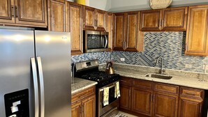 A kitchen with wooden cabinets, stainless steel appliances, a tiled backsplash, and two kitchen mats on the floor.