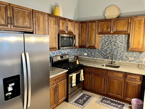 A kitchen with wooden cabinets, stainless steel appliances, a tiled backsplash, and two kitchen mats on the floor.
