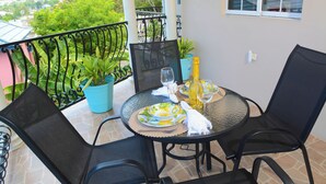 A balcony with a table set for two, featuring a glass top, two chairs, a bottle of champagne, and a wine glass.