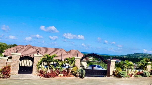 A gated residential area with a two-story house, a driveway, and a view of the surrounding landscape.