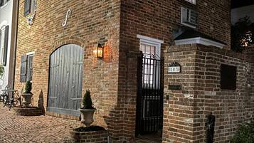 Un edificio de ladrillo con una gran puerta de madera, un pequeño jardín con plantas en macetas y una señal de calle que dice 'Private Alley'.