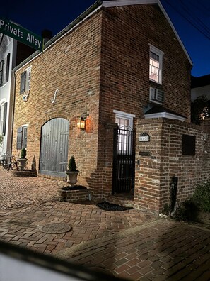 A brick building with a large wooden door, a small garden with potted plants, and a street sign reading 'Private Alley'.