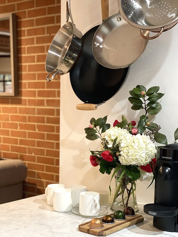Un comptoir de cuisine avec une machine à café, un vase rempli de fleurs et, en arrière-plan, un mur en briques.