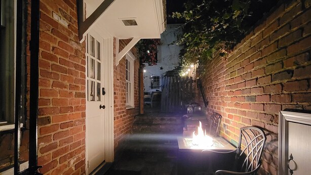 Une ruelle étroite en briques, avec une porte blanche, un banc et une petite table sur laquelle brûle une bougie.