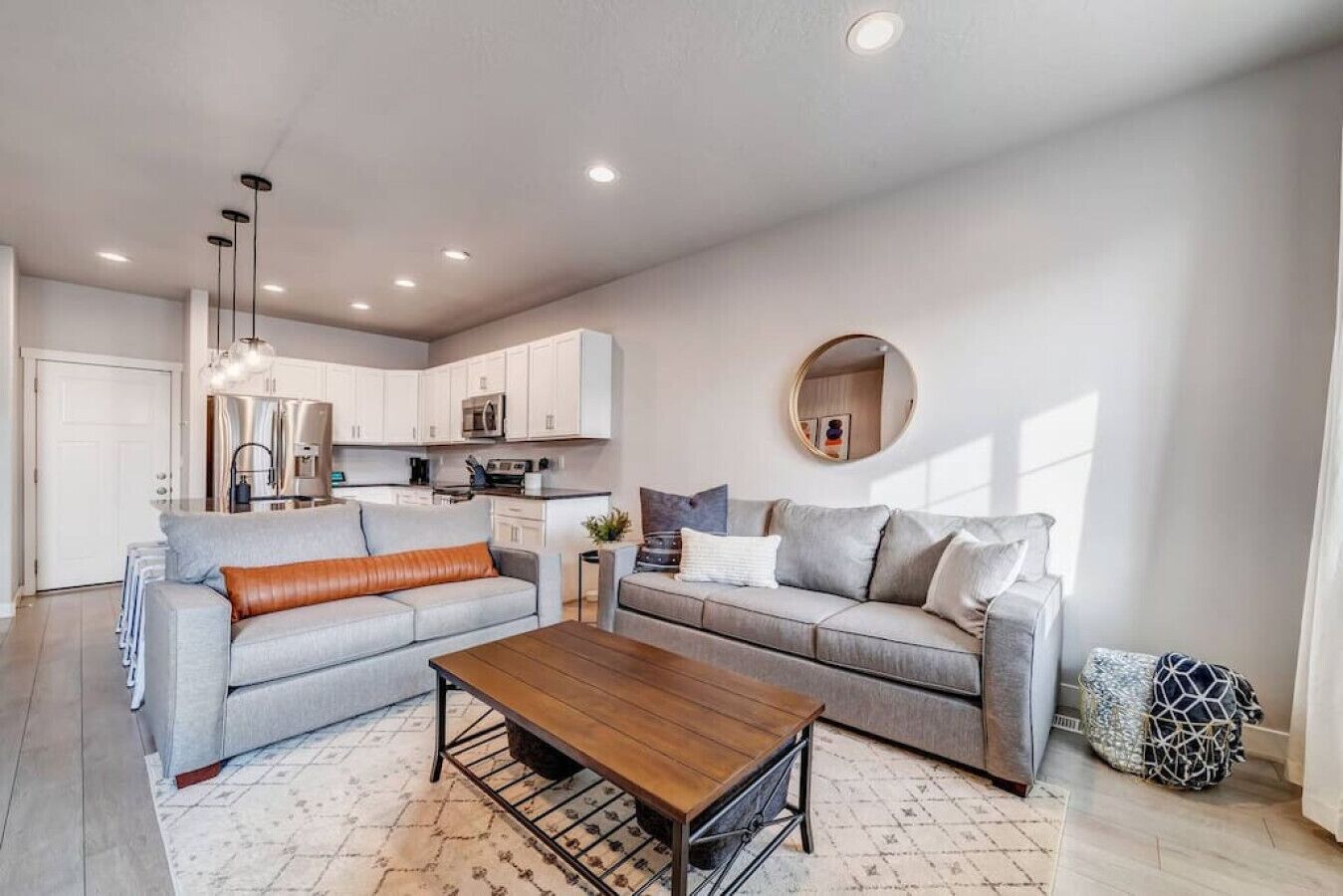 A modern living room with a grey sofa, a wooden coffee table, and a kitchen in the background.