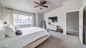 Ein Schlafzimmer mit einem Bett, einem Deckenventilator, einem Fernseher, einer Kommode und einem Fenster.