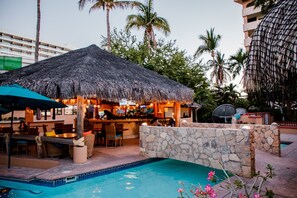 A poolside bar area with a thatched roof, stone walls, and outdoor seating. - BEAUTIFUL CONDO 2 BD 5 MIN WALKING FROM BEACH AND DOWNTOWN (Cabo San Lucas)