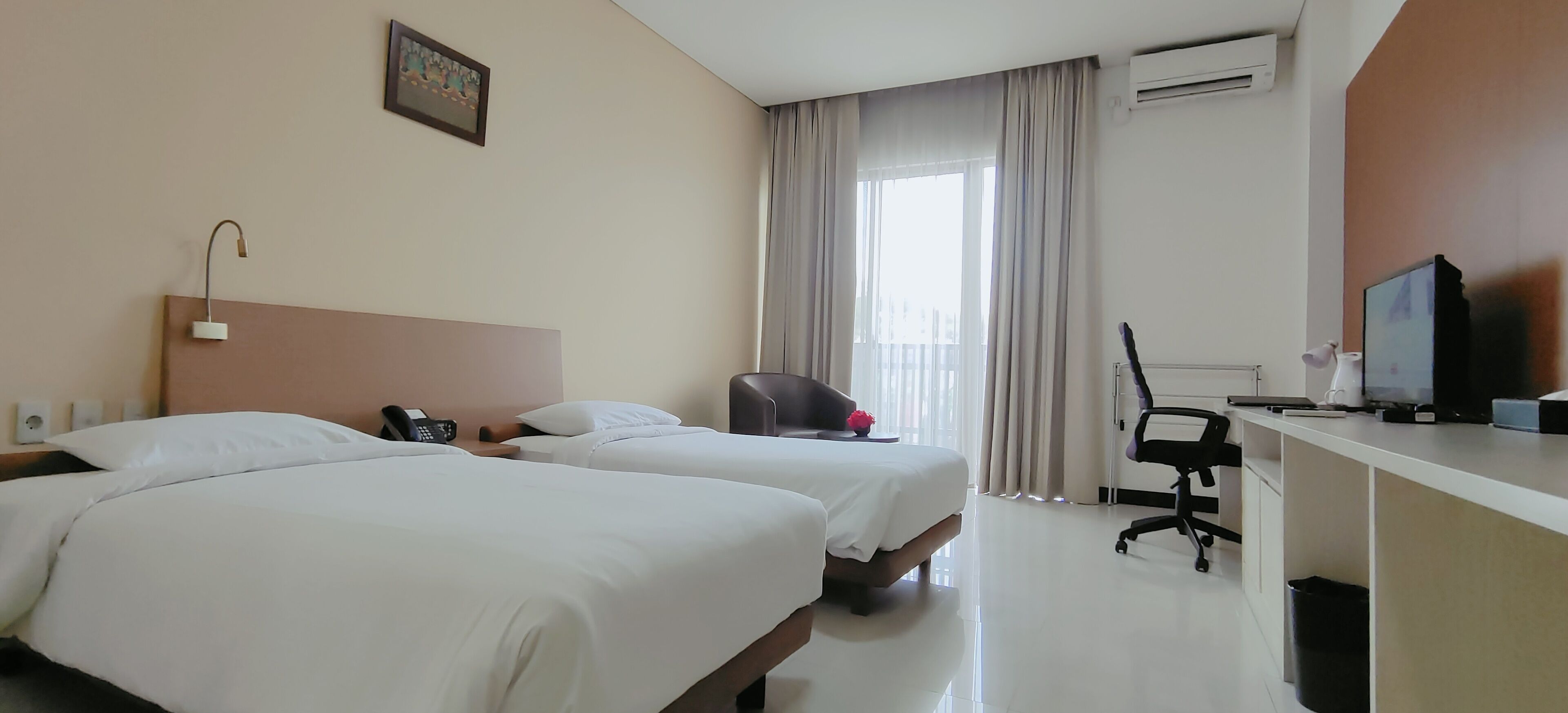 Ein Hotelzimmer mit zwei Betten, einem Schreibtisch, einem Computer, einem Stuhl und einem Fernseher.