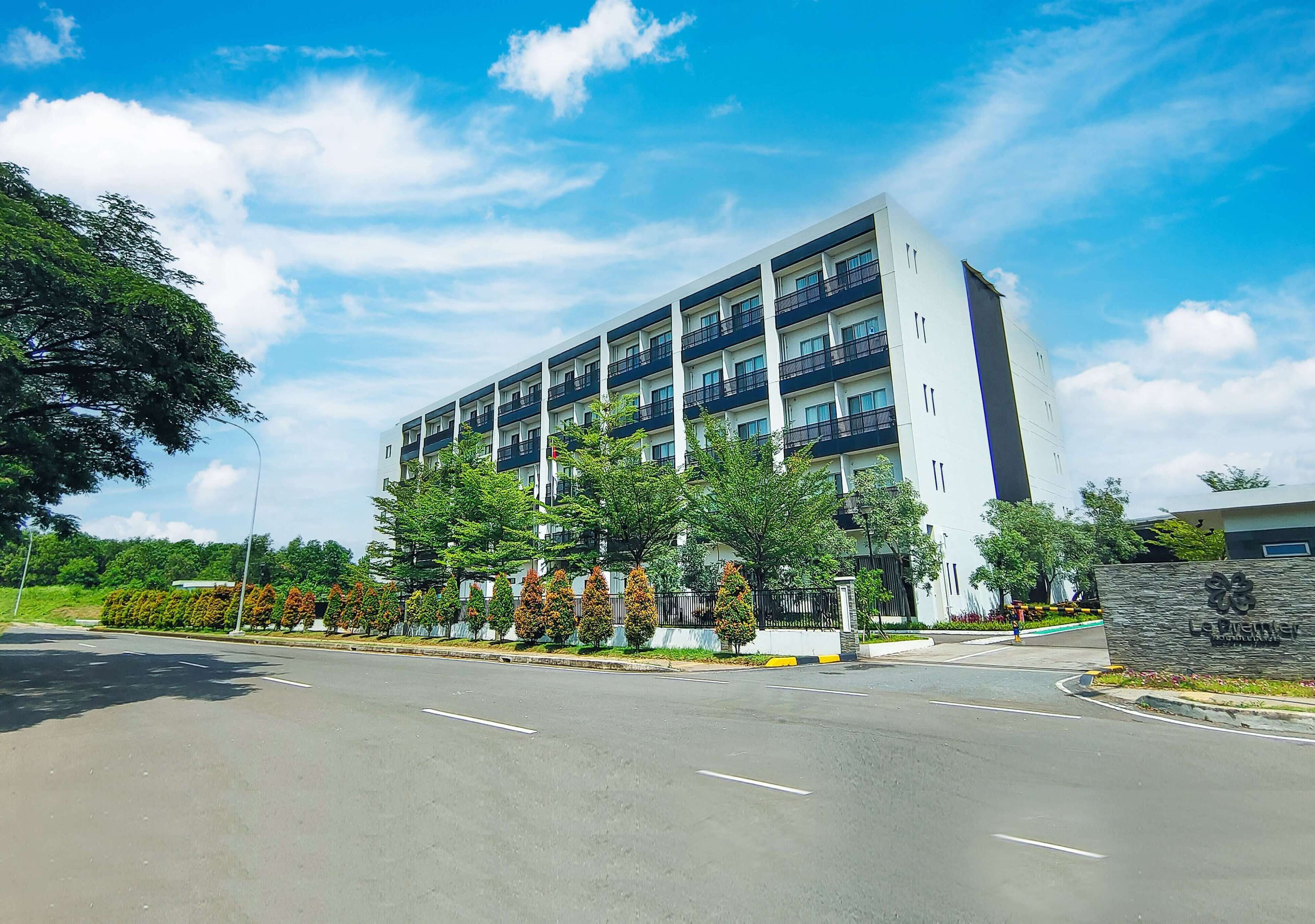 A multi-story hotel with a modern design, featuring balconies on each floor and a landscaped entrance area.