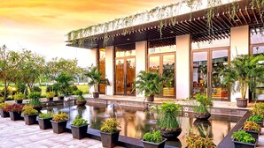 A modern hotel with a pool, potted plants, and a covered outdoor area.