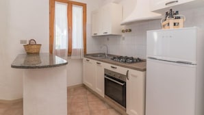 A compact kitchen with a gas stove, oven, and white refrigerator. - Rubinia by Interhome (Valledoria)
