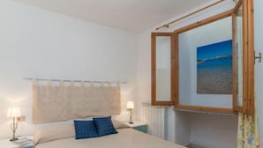 A bedroom with a bed, two bedside lamps, a window with a view of the beach, and a curtain. - Rubinia by Interhome (Valledoria)